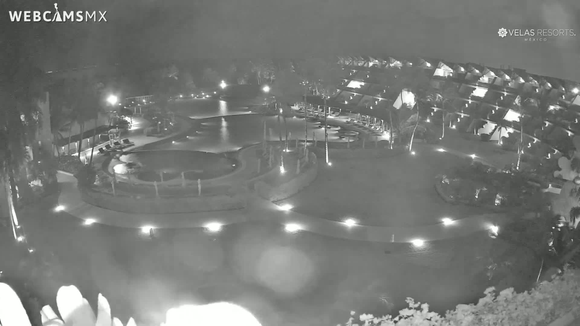 A nighttime, aerial view of a resort with a swimming pool and surrounding buildings, illuminated by lights.