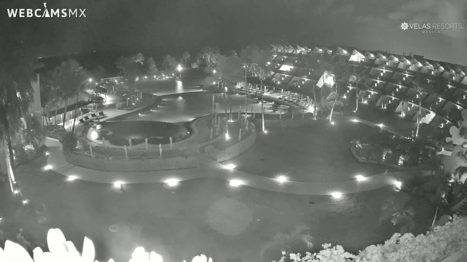 A nighttime aerial view of a resort with a winding pool and surrounding buildings, lit by ambient lighting.