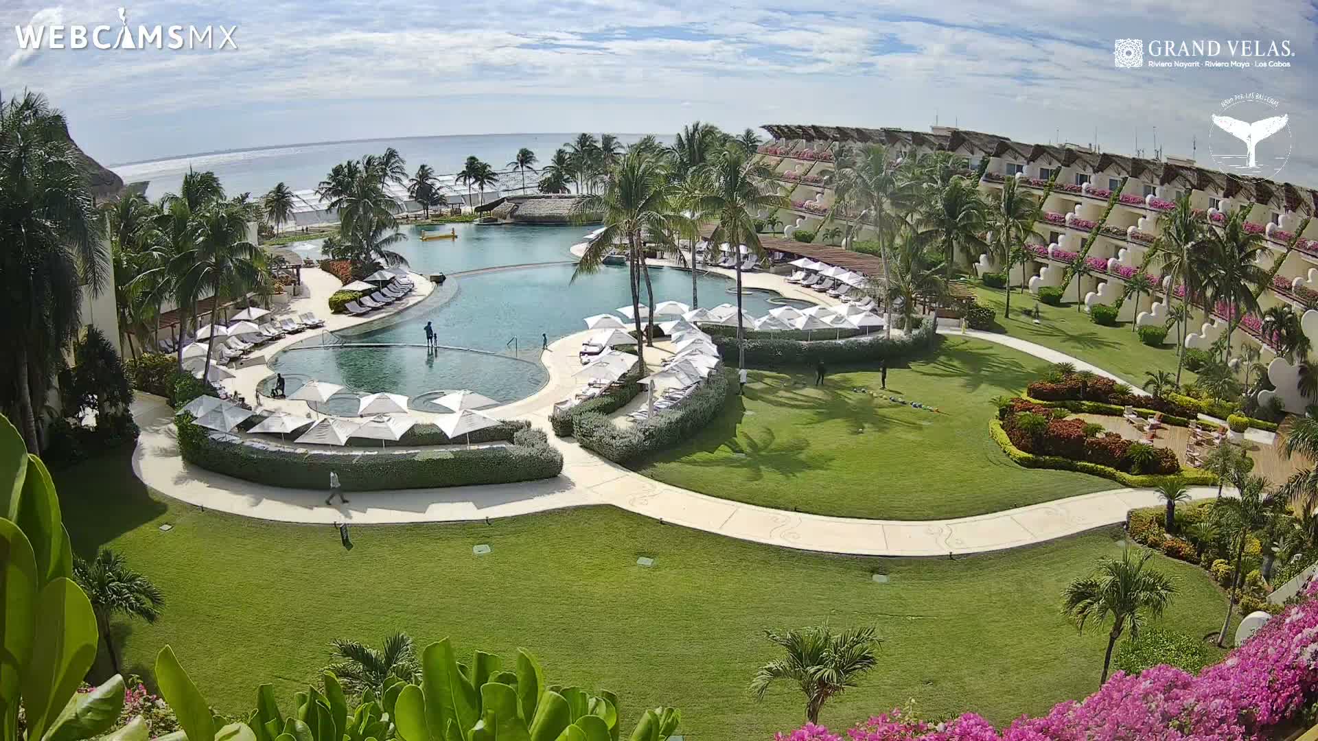 A nighttime, low-light aerial view shows a resort with a large pool and numerous buildings illuminated by scattered lights.