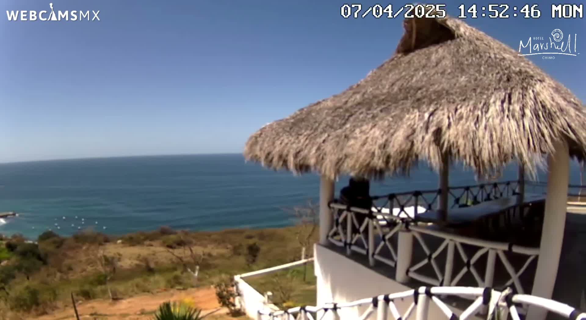A thatched-roof gazebo overlooks a calm ocean under a clear blue sky.