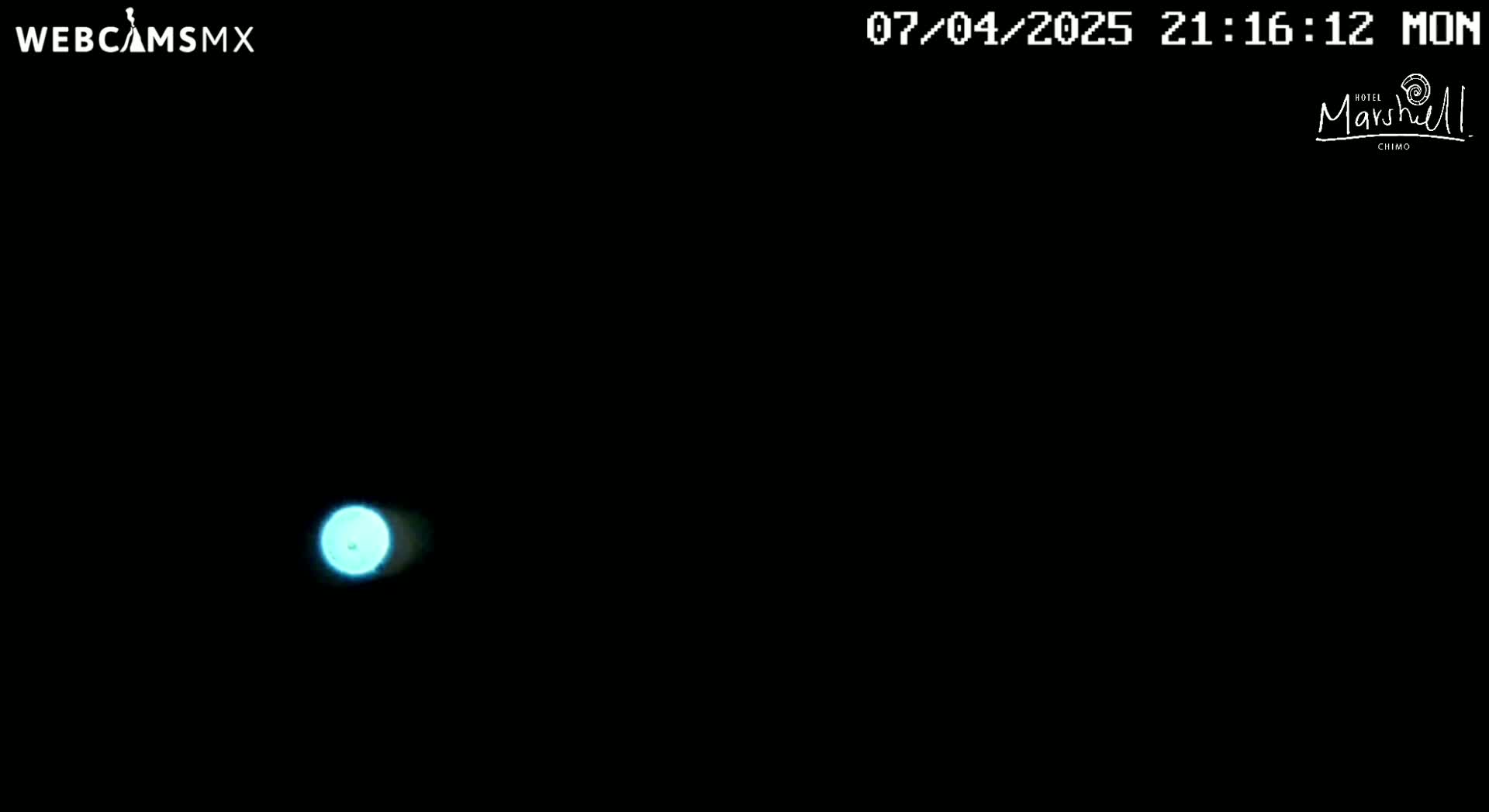 A small, bright cyan light is visible in the center of a dark, nighttime scene.