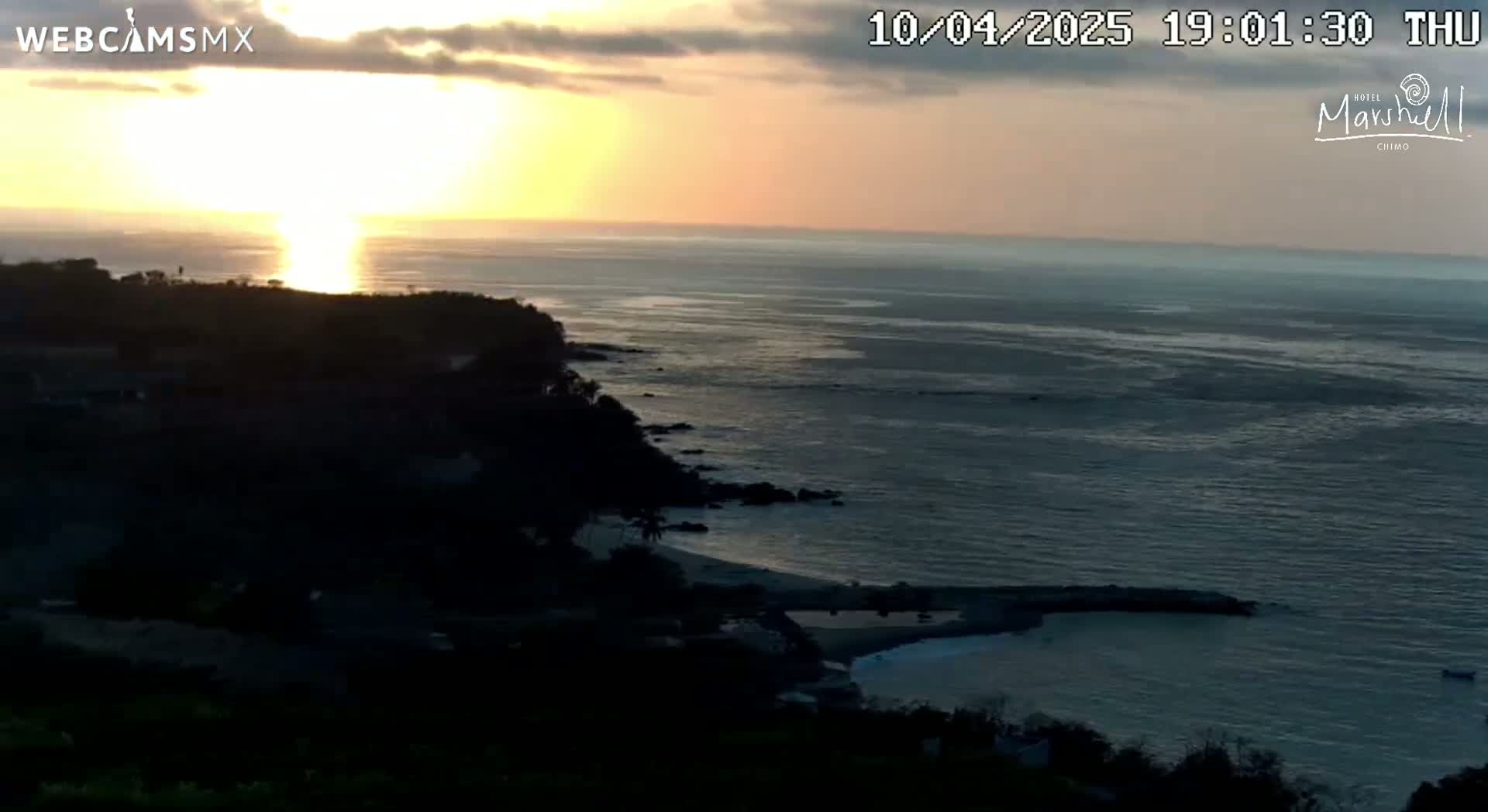 A sunset over a dark, rocky coastline and calm ocean.