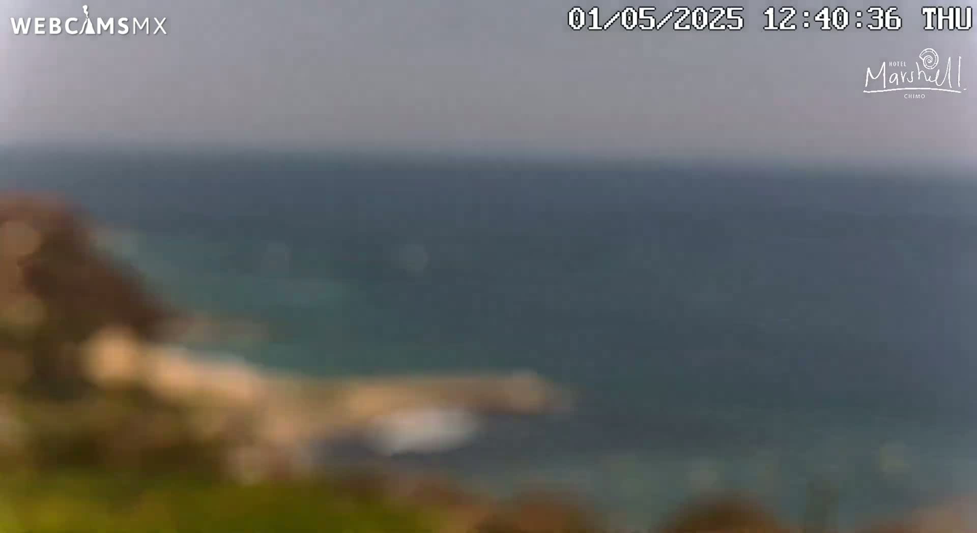 A blurry image shows a hazy, overcast day with a calm body of water and indistinct land features in the foreground.