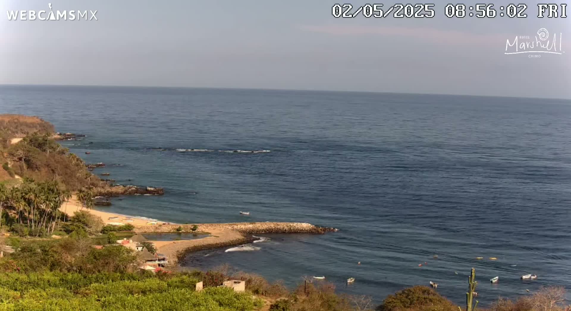 A high-angle view shows a rocky coastline with a small beach and calm ocean under a clear sky.