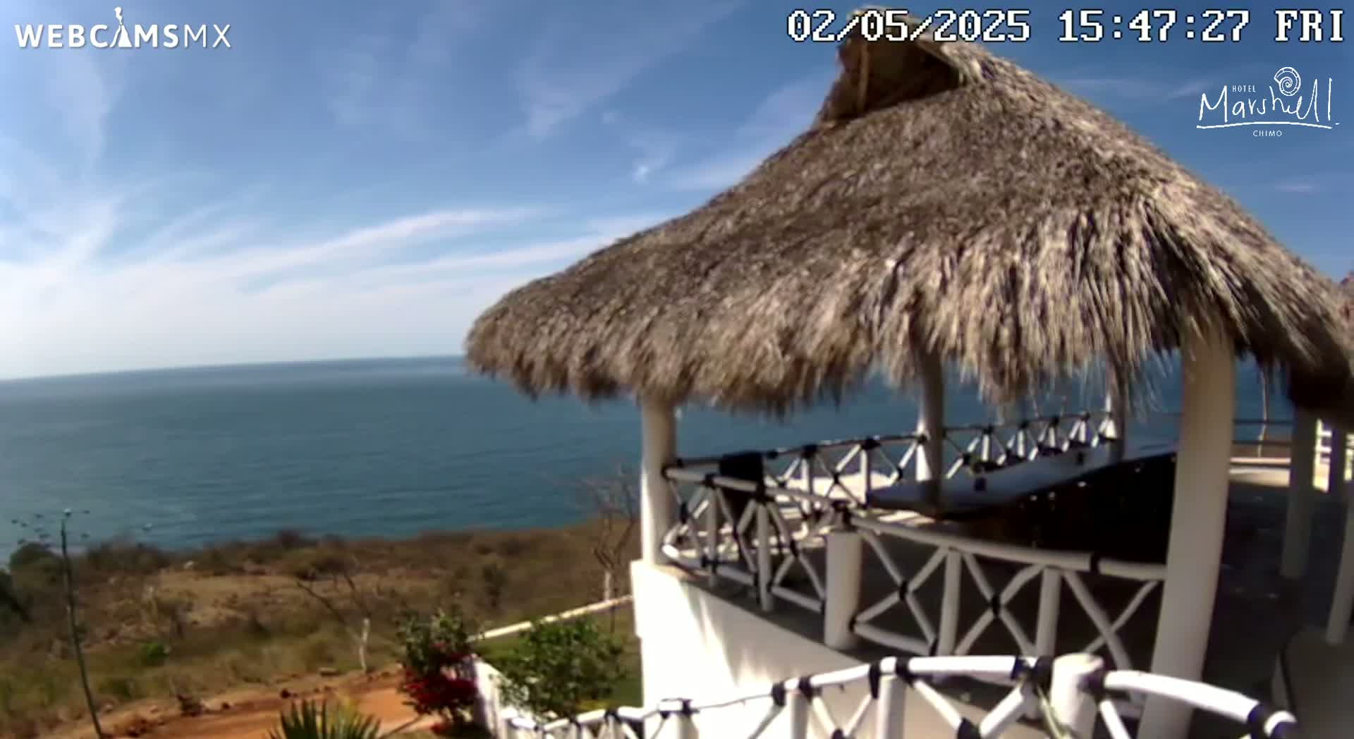 A thatched-roof gazebo overlooks a calm ocean under a mostly sunny sky.