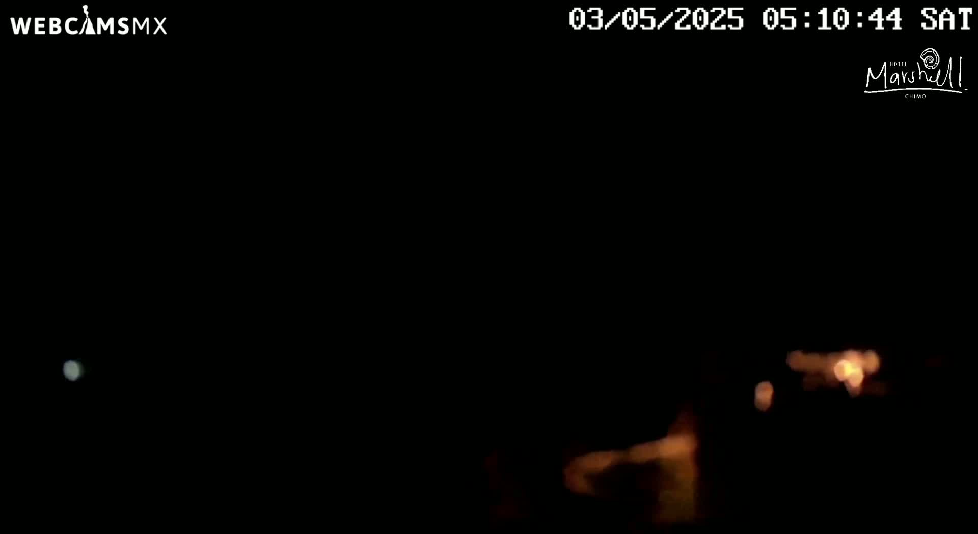 A nighttime, blurry view shows a faint light in the distance and some brighter lights closer, possibly indicating buildings or other structures.