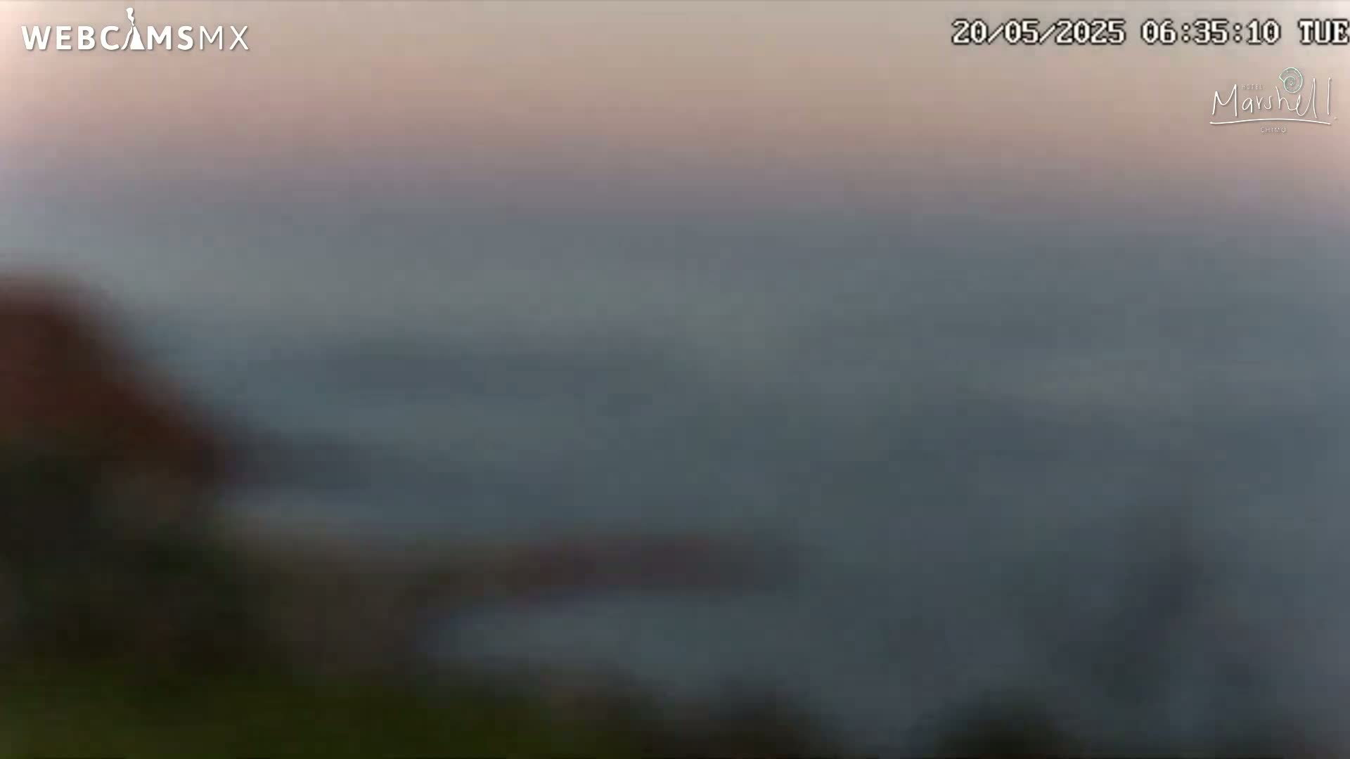 A blurry, out-of-focus image shows a hazy, grayish-blue body of water under a pale, pinkish-orange sky at dawn or dusk.