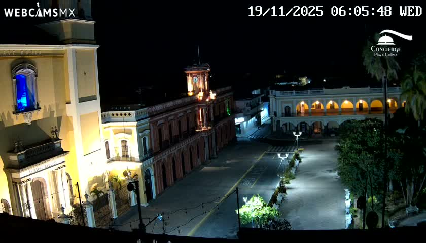 A sunny, outdoor view of a town square, featuring a large church, colonial-style buildings, lush green trees, and an outdoor patio area with tables and chairs.