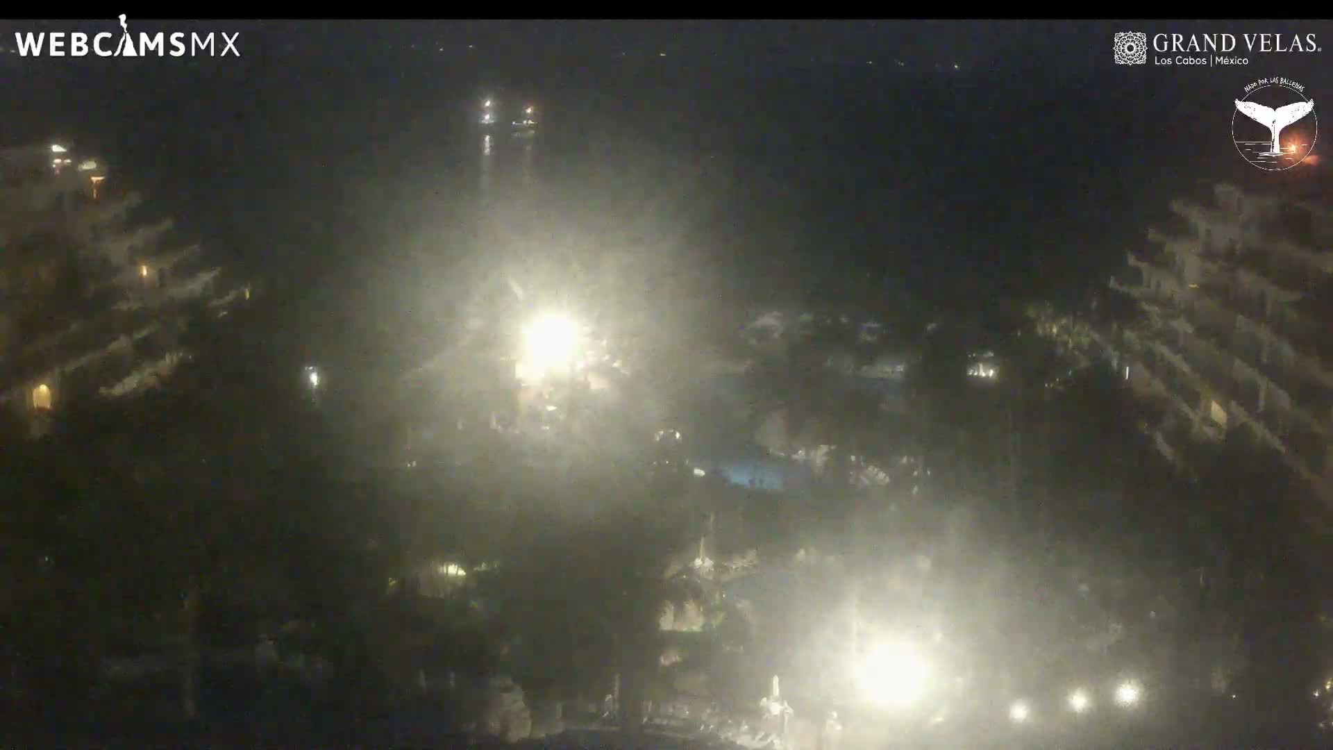 A hazy night scene shows a resort complex with pools and buildings illuminated by lights.