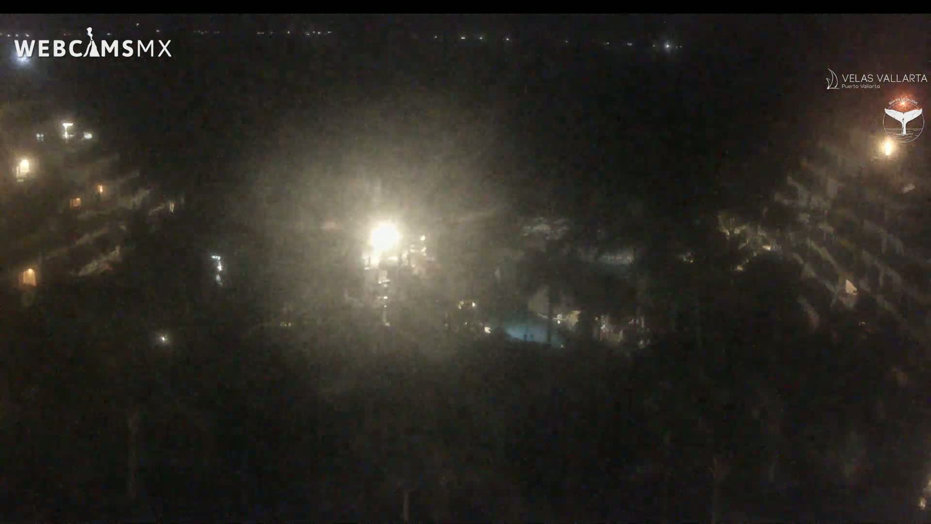 A nighttime, hazy view of a resort complex with dimly lit buildings and a pool area.