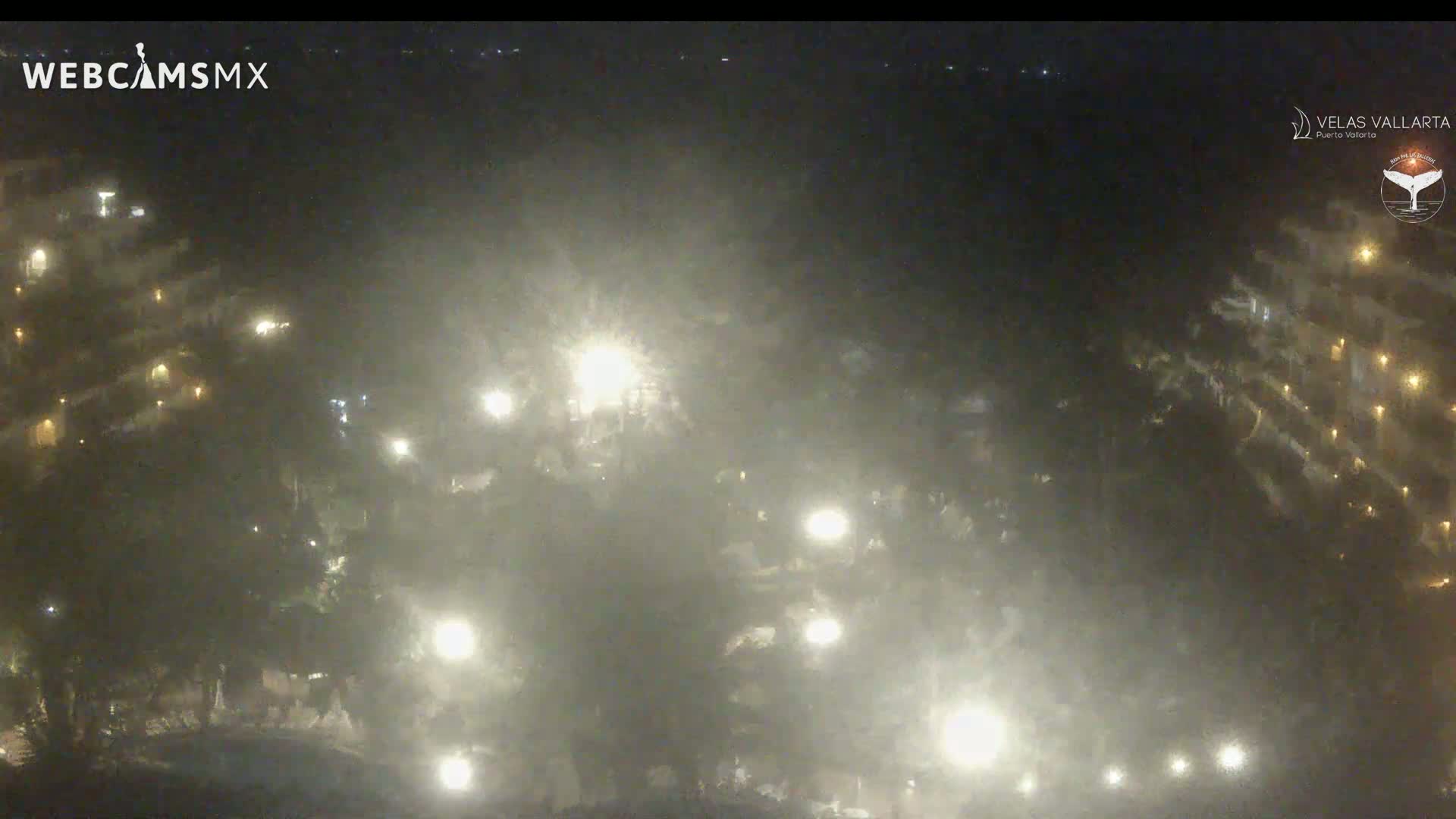 A hazy night scene shows a multi-story building with lights on, partially obscured by fog or mist.