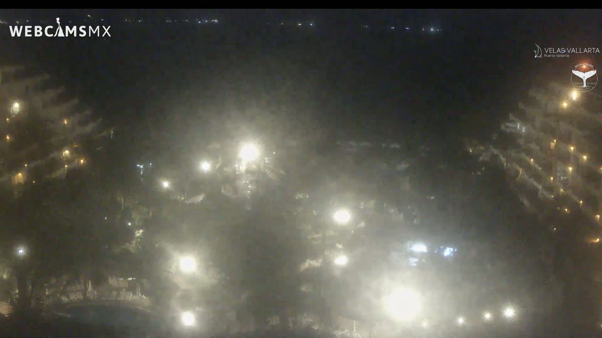 A hazy night scene shows a resort area with buildings and landscaping illuminated by numerous lights.