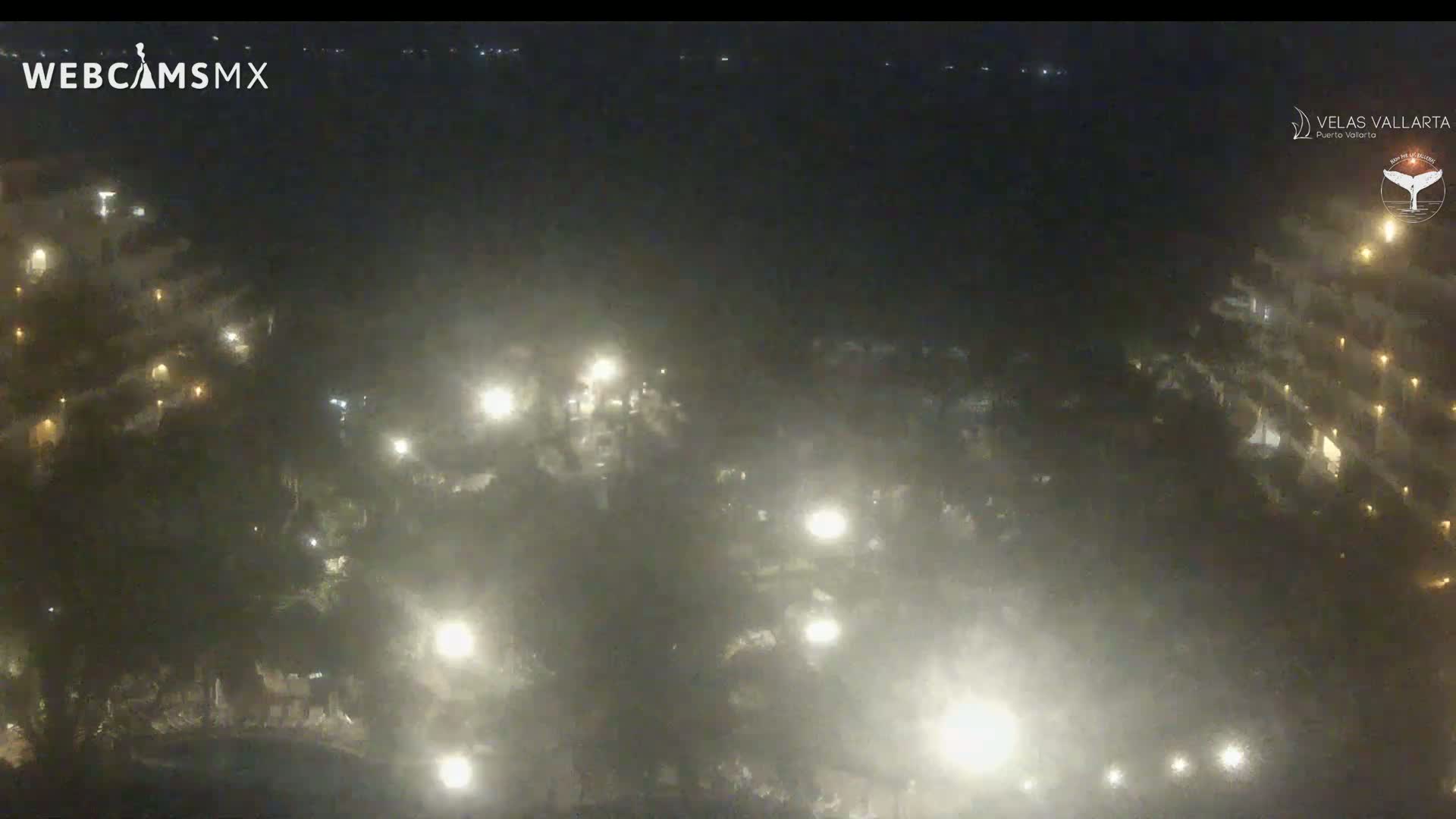 A hazy night scene shows numerous lights illuminating a resort area with buildings partially visible.