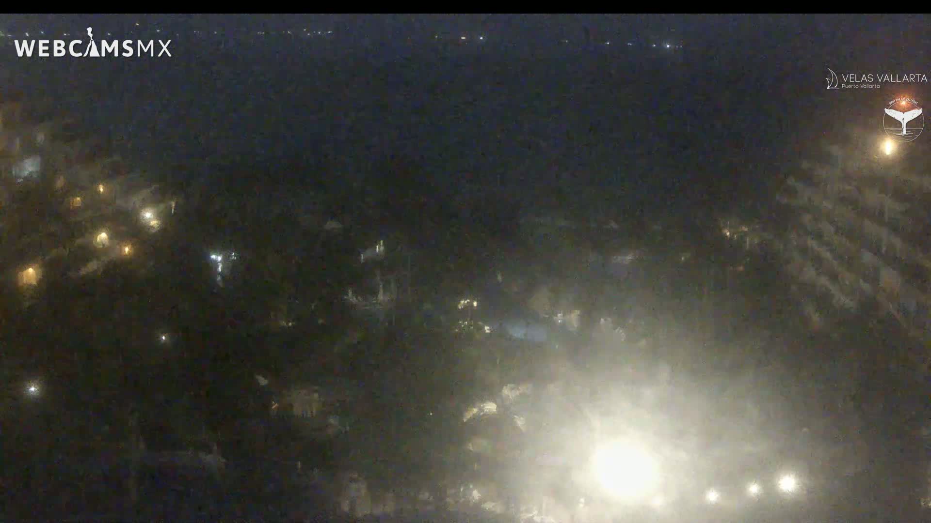 A nighttime, hazy view of a resort area with scattered lights and a body of water in the distance.