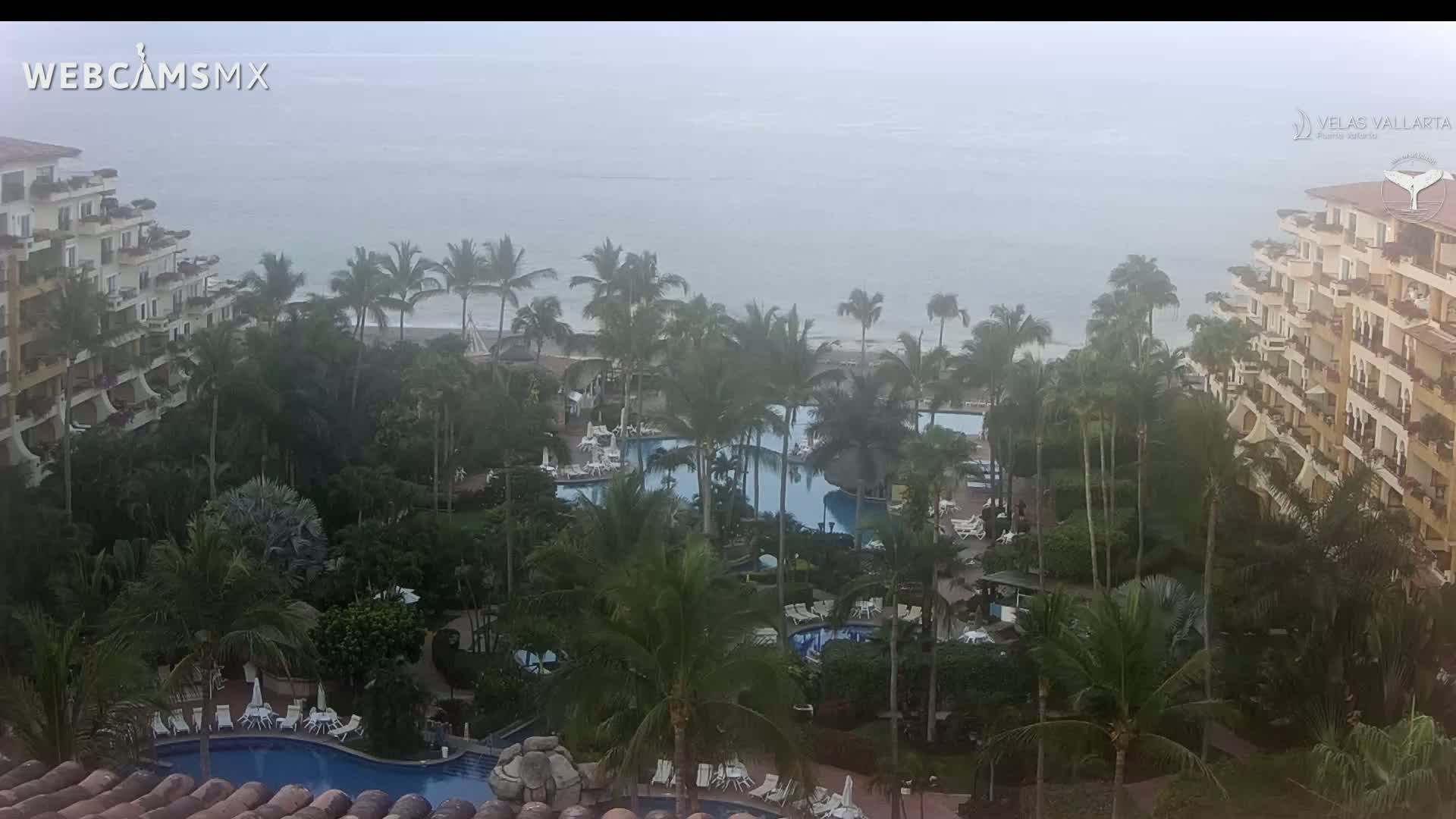 A hazy, misty view of a tropical resort with multiple pools surrounded by palm trees and buildings overlooking the ocean.