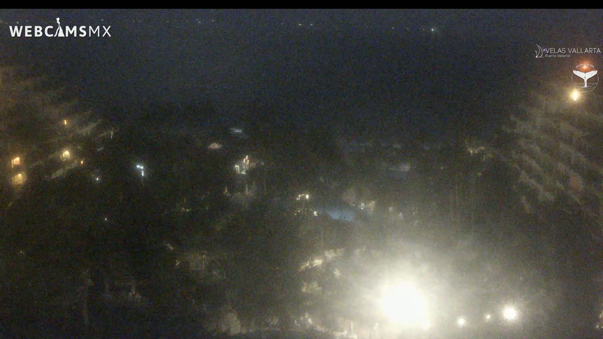 A nighttime aerial view of dimly lit buildings and vegetation under hazy or foggy conditions.