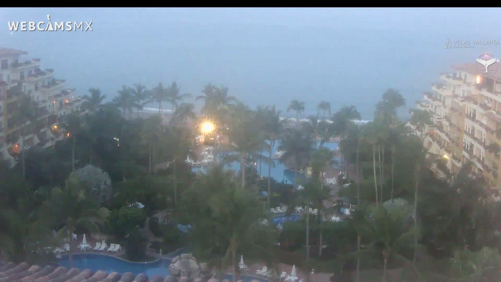 A hazy, overcast day reveals a resort with multiple pools and palm trees surrounding large buildings near the ocean.