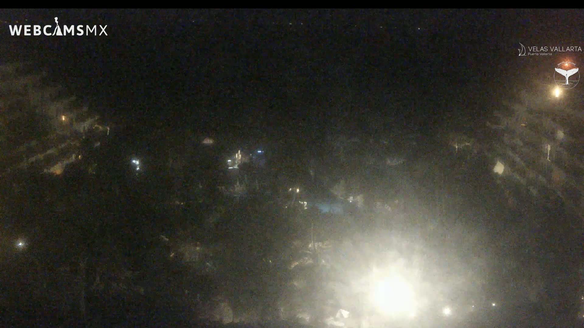 A nighttime, hazy aerial view shows a collection of dimly lit buildings and structures.