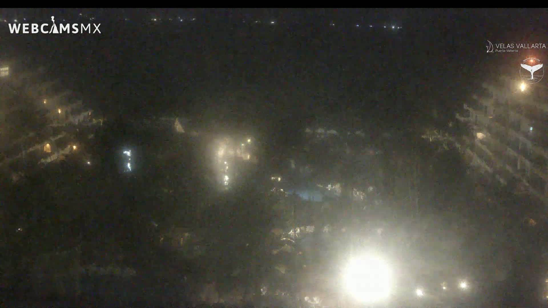 A hazy night scene shows a dark, low-lit resort area with some lights visible from buildings and possibly pools.