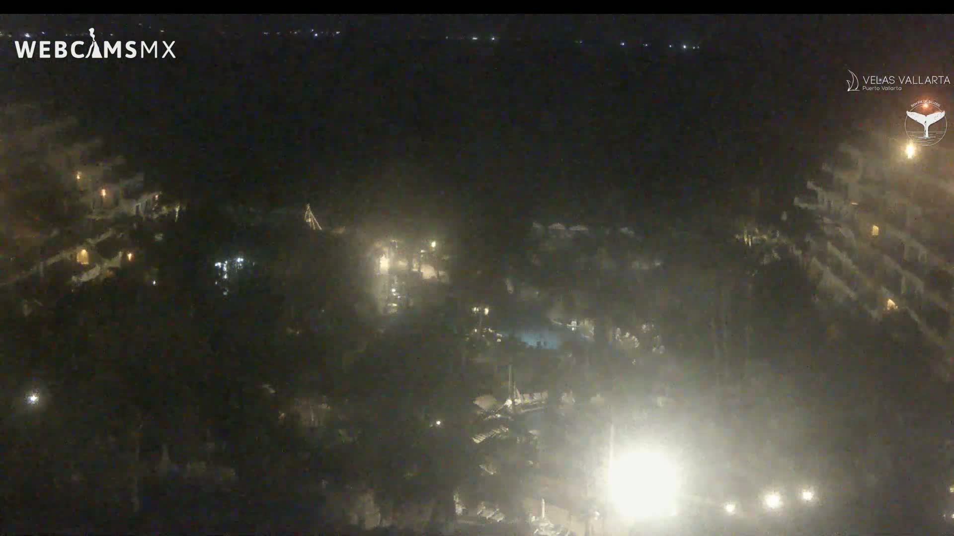 A nighttime, hazy view from above shows a resort area with buildings and pools illuminated by scattered lights.