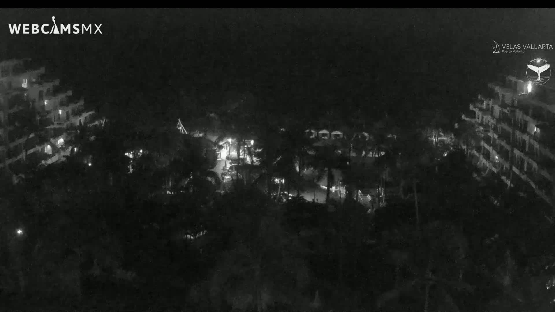 A nighttime, aerial view shows a resort complex with dimly lit buildings and palm trees.