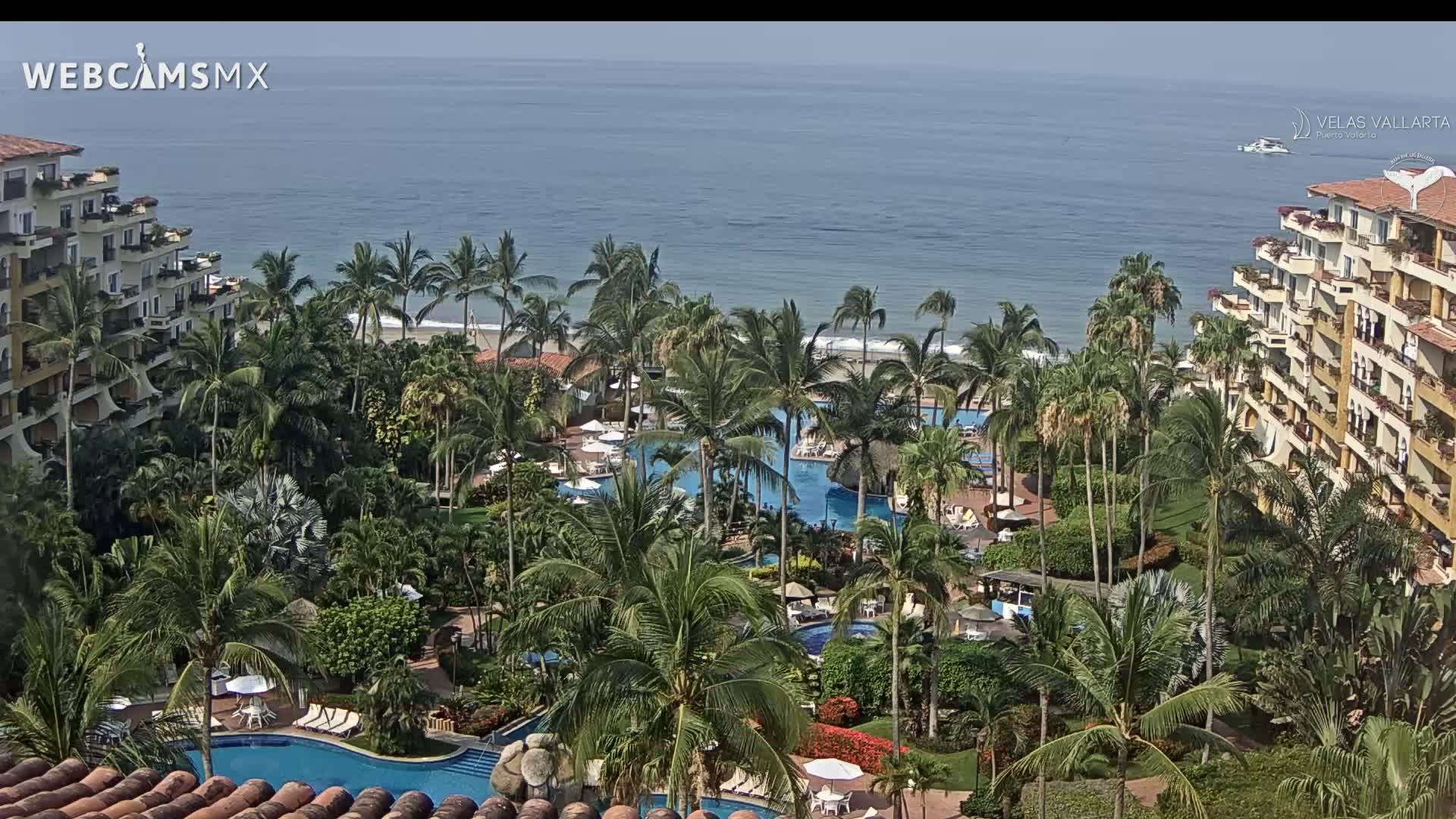 A resort with multiple pools is nestled among lush tropical vegetation, overlooking a calm ocean under a clear sky.