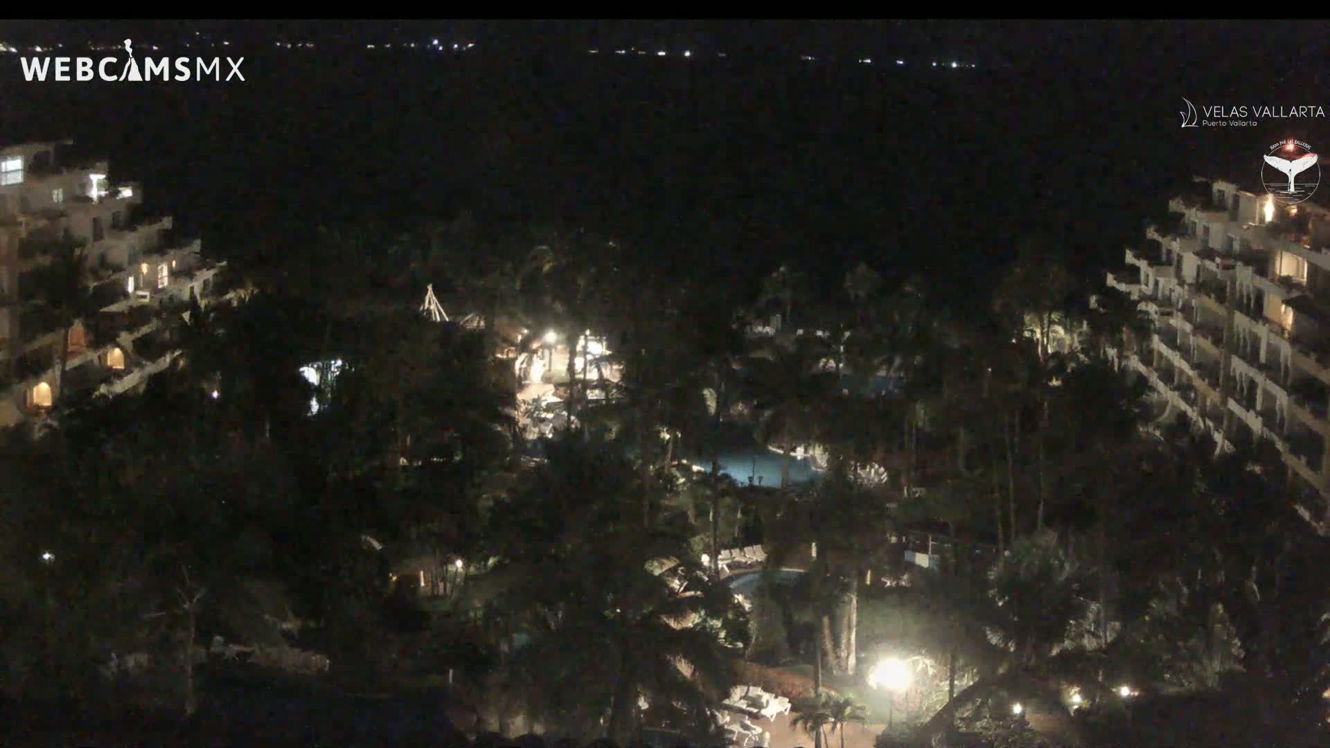 A nighttime aerial view of a resort complex with swimming pools, palm trees, and buildings illuminated by lights.