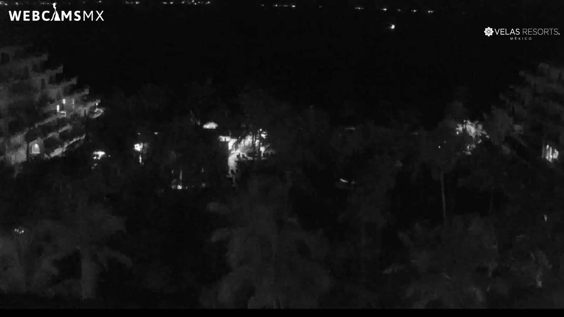 A nighttime view of a resort with multiple buildings, lush tropical landscaping, and illuminated pools.