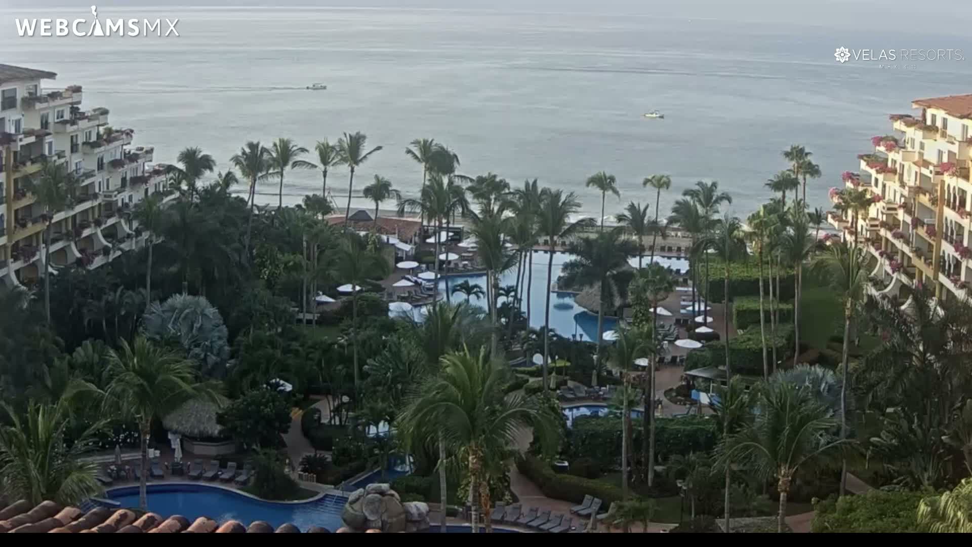 An elevated nighttime view reveals a brightly lit tropical resort complex featuring multiple buildings, palm trees, and swimming pools under a clear, dark sky.