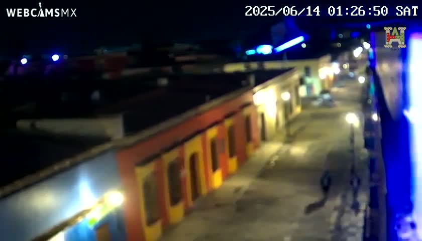 A nighttime, high-angle view shows a street lined with brightly lit, colorful buildings.