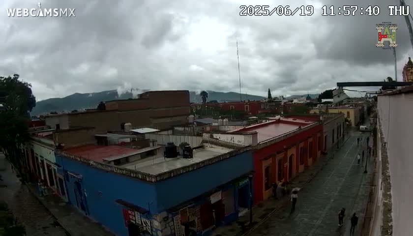A street scene shows a row of colorful buildings under an overcast sky, with mountains visible in the distance.