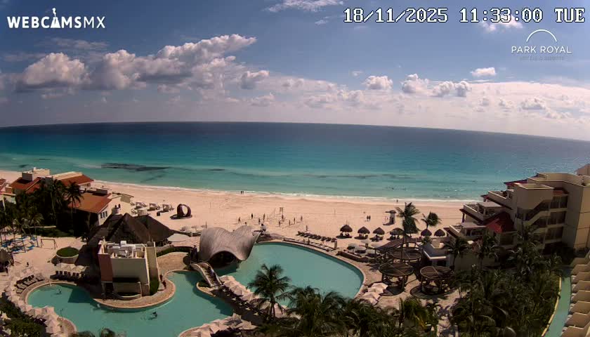 A cobblestone plaza, bordered by colonial-style buildings, with a few pedestrians and small trees, under an overcast sky.