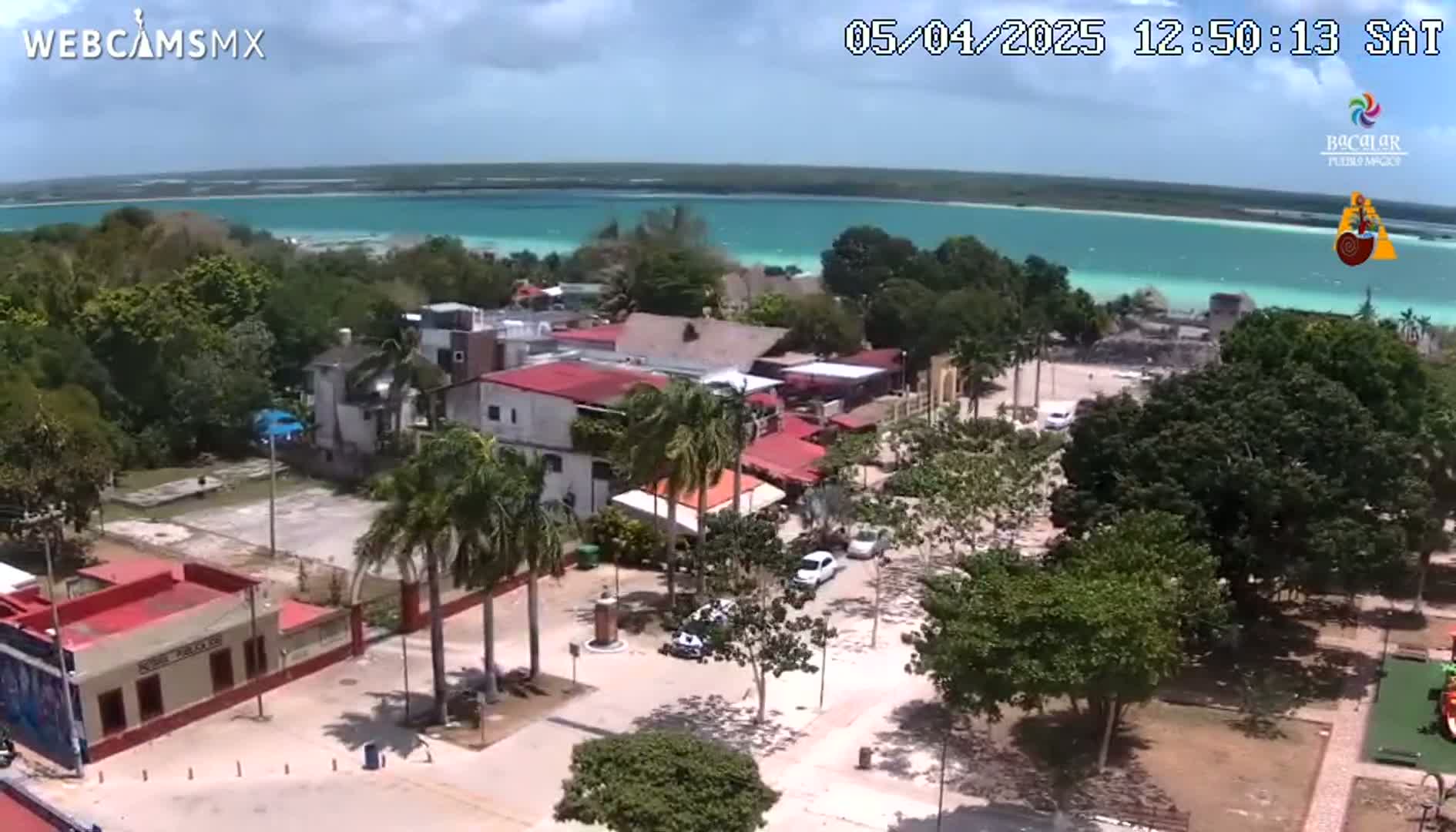 An aerial view of a town situated next to a turquoise body of water under partly cloudy skies.