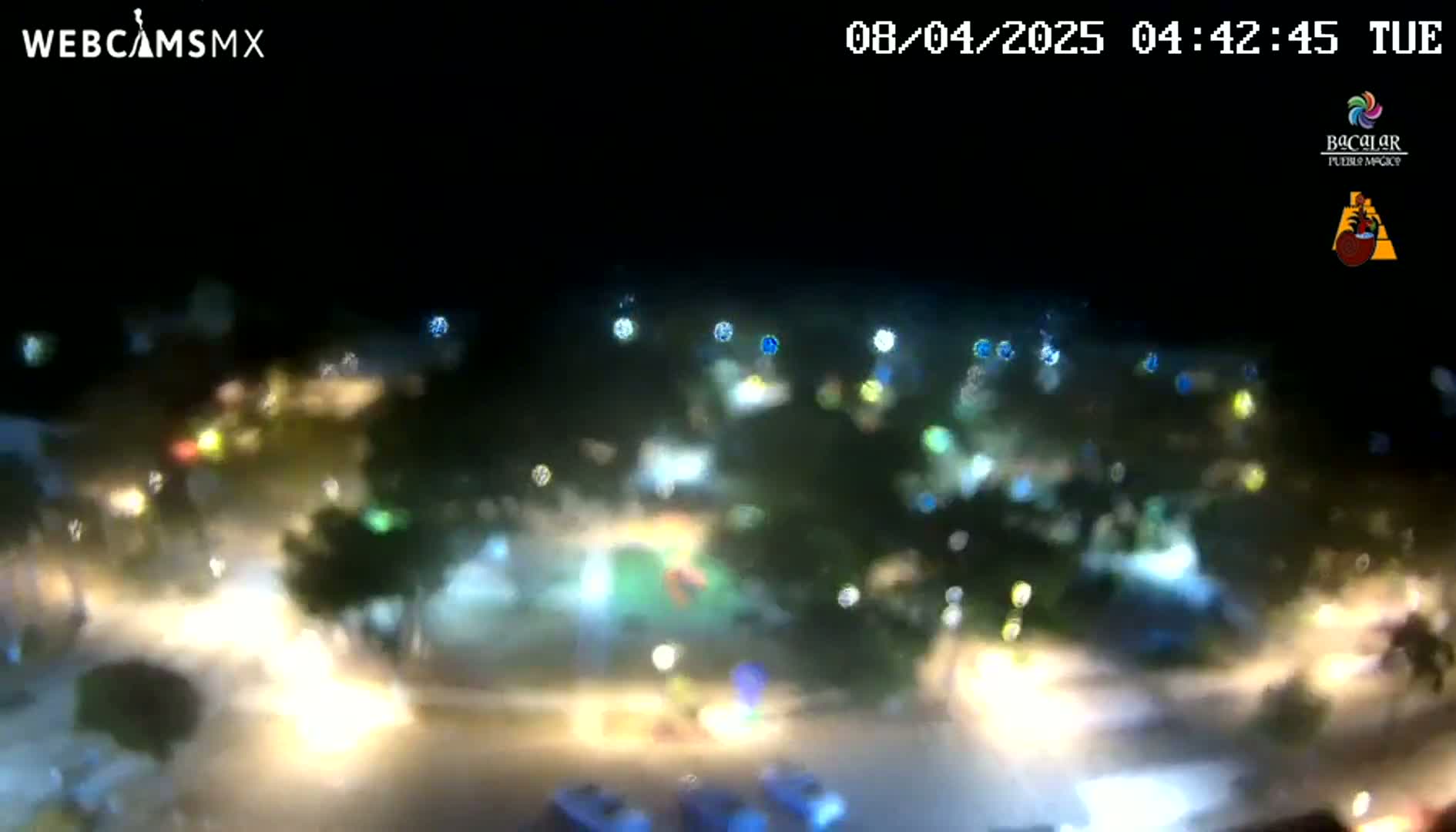 A blurry nighttime aerial view of a rain-soaked area shows numerous lights from vehicles and streetlights.