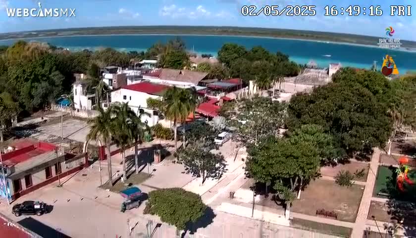 An aerial view shows a town situated beside a calm, turquoise body of water under a partly sunny sky.