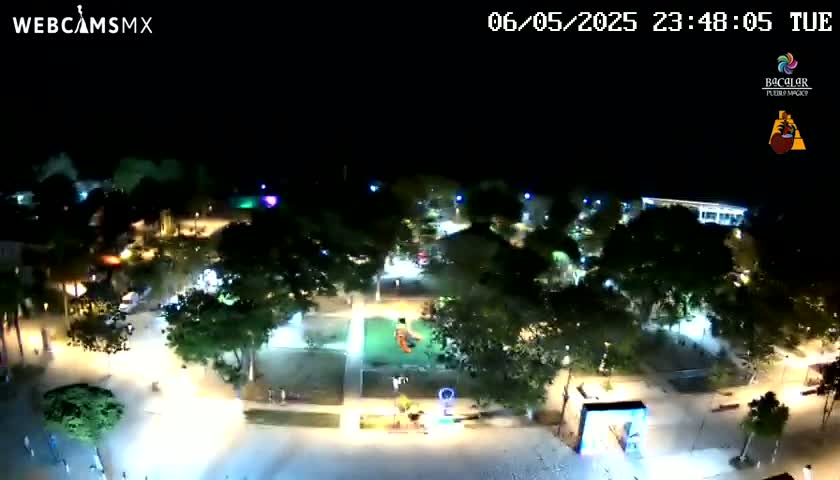 A nighttime aerial view of a brightly lit plaza with trees and people, under a clear sky.