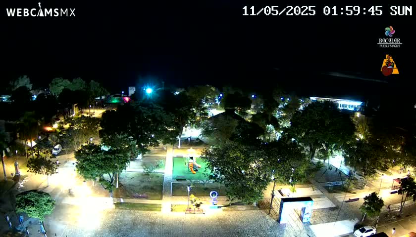 A nighttime aerial view of a park with illuminated pathways and trees, under a clear sky.