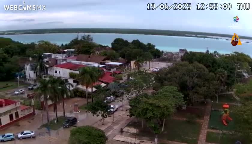 An aerial view shows a town with flooded streets near a calm body of water under an overcast sky.