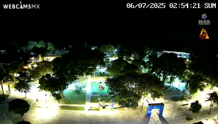 An illuminated park at night, filled with trees and pathways, shows a playground in the center.