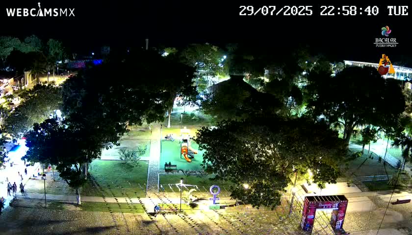 A nighttime aerial view of a town square with buildings, trees, and illuminated streets.