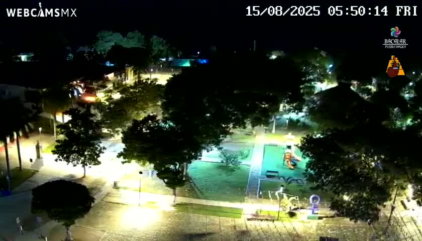 A nighttime aerial view of a town square with buildings, trees, and illuminated streets.