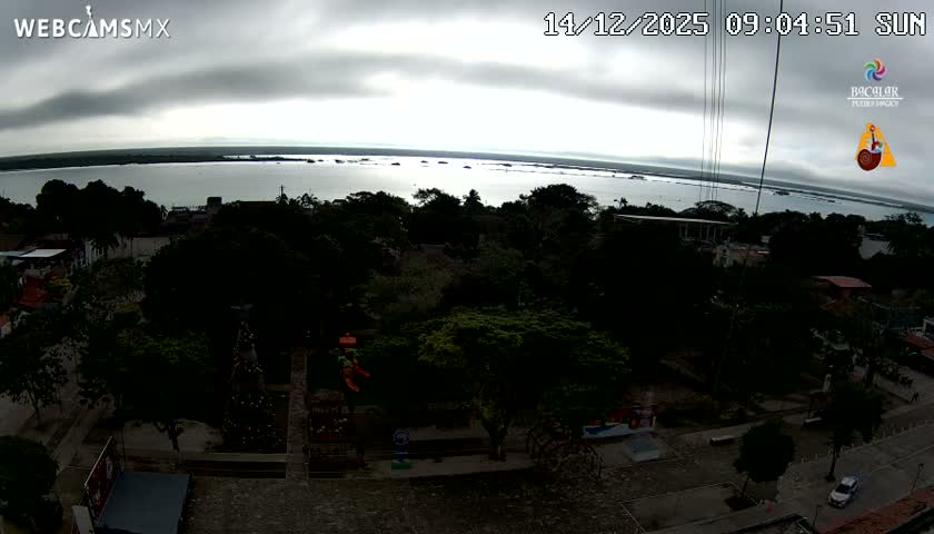 A clear night illuminates an outdoor town square or park with trees, pathways, a playground, and distant buildings under artificial lighting.