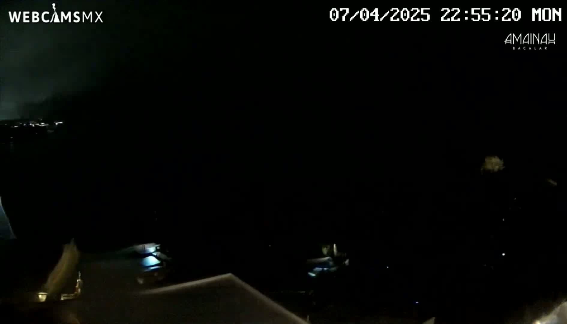 A nighttime, dark scene shows a partially visible surface and a dark, unclear background with a few small lights visible in the distance.