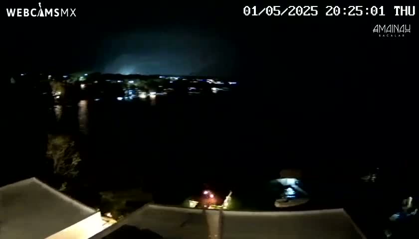 A nighttime view of a body of water with a town in the distance under a dark, possibly stormy sky.