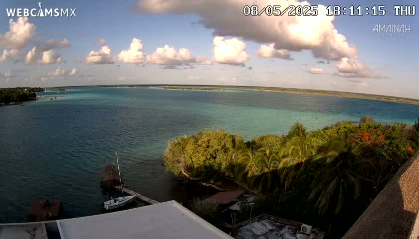 A partly cloudy afternoon view of a calm body of turquoise water, tropical vegetation, and a few boats near a shoreline.