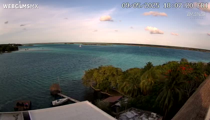 An elevated view shows a calm body of turquoise water under a partly cloudy sky, with tropical vegetation and boats in the foreground.