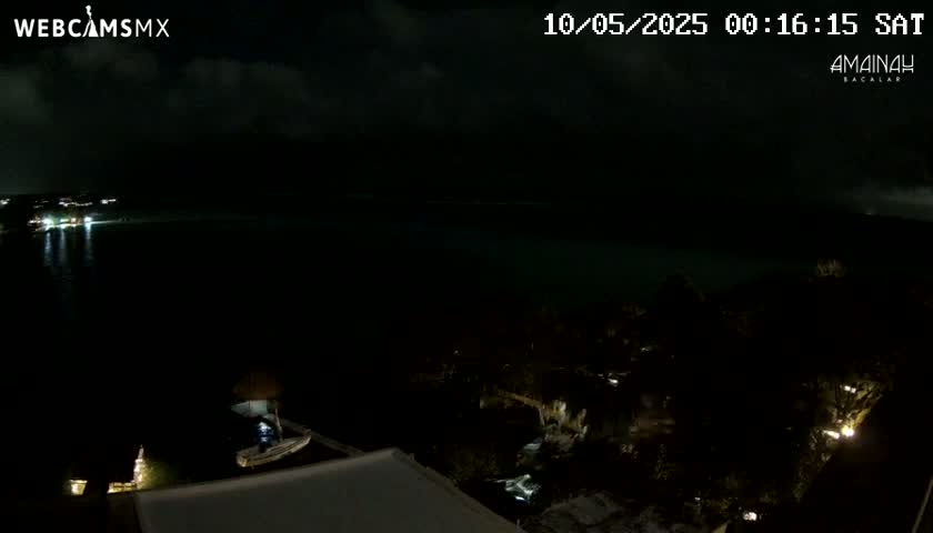 A nighttime view of a dark body of water with a few lights visible on the opposite shore under a partly cloudy sky.