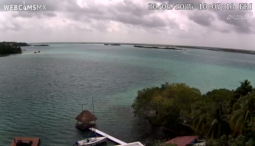 A tranquil body of teal water under a cloudy sky, shows small islands in the distance, boats at a dock, and lush green vegetation along the shore.