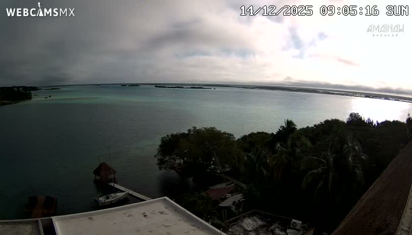 A very dark outdoor night scene reveals a few faint distant lights scattered across the horizon and a partially visible structure in the foreground, under clear skies.