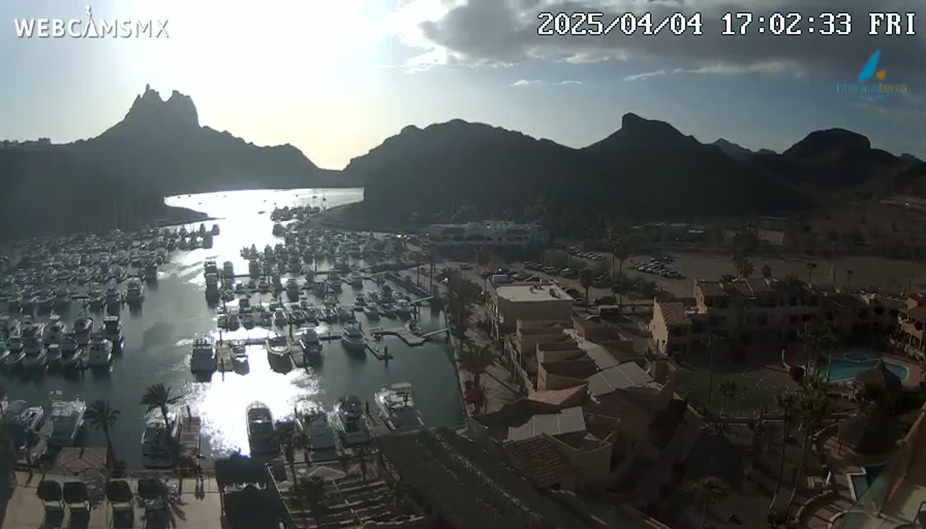A partly cloudy day reveals a marina filled with numerous boats nestled against a backdrop of mountains.